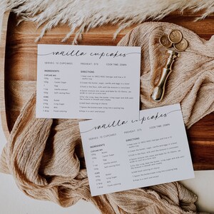 K&ouml;nnte beinhalten: Zwei Rezeptkarten f&uuml;r Vanille-Cupcakes werden auf einem Holztablett mit einem beigen Tuch pr&auml;sentiert. Die Karten enthalten handschriftlichen Text mit Zutaten und Anweisungen. Ein goldfarbener Wachssiegelstempel ist ebenfalls vorhanden.