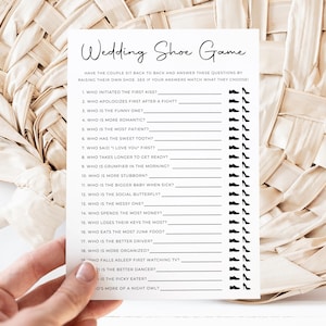 May include: A white rectangular card titled Wedding Shoe Game with black text and graphics. The card lists twenty questions with lines for answers, each accompanied by a small black icon of a dress shoe and a high heel shoe for selection.