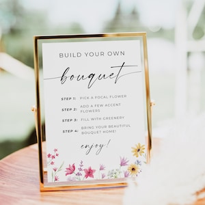 May include: A gold-framed sign with the text "BUILD YOUR OWN bouquet" and instructions for creating a bouquet. The sign includes steps like picking a focal flower and adding greenery. Floral illustrations decorate the bottom.