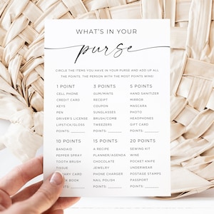Peut inclure: Une carte blanche avec du texte noir qui dit "What's in your purse?" et liste des articles avec des points attribués à chacun. Les articles comprennent des objets courants dans un sac à main comme un téléphone portable, du chewing-gum, du désinfectant pour les mains et du rouge à lèvres. La carte est tenue dans une main contre un fond tissé.