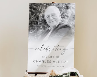 Könnte beinhalten: Gedenktafel auf einer Holzstaffelei. Das Schild zeigt ein Schwarz-Weiß-Porträt eines Mannes mit dem Text "Celebrating The Life of Charles Albert" und Datumsangaben. Die Staffelei ist mit Grün und Stoff dekoriert.