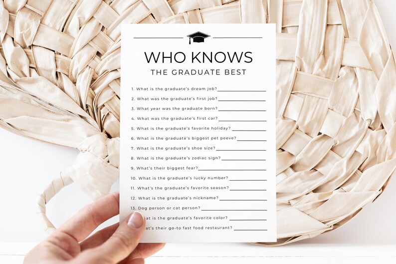 Op de afbeelding: Een witte kaart met de tekst "WHO KNOWS THE GRADUATE BEST" en invulvragen over de afgestudeerde. De kaart wordt door een hand vastgehouden en tegen een geweven achtergrond geplaatst. De kaart bevat een afstudeerpet-afbeelding.