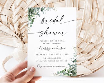 May include: A white invitation card with the words "bridal shower" in elegant script. The card includes details like the date, time, and location, with floral accents. The card is held by a hand against a woven background.