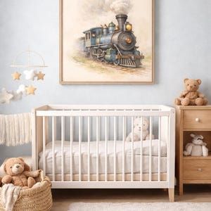 Könnte beinhalten: Ein gerahmter Aquarelldruck eines blauen und schwarzen Dampfzuges aus der Zeit hängt über einem weißen Kinderbett in einem Kinderzimmer. Der Raum ist mit einem Mobile, einem Weidenkorb mit einem Teddybär und einer Holzkommode dekoriert.