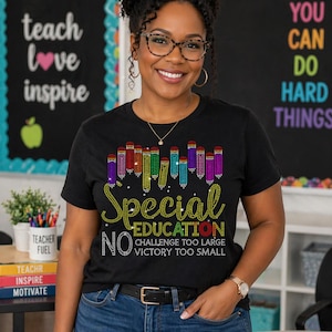 May include: A black t-shirt with the words "Special Education" in a rhinestone design, along with colorful rhinestone pencils. The shirt also has the phrases "No Challenge Too Large, Victory Too Small". The person is wearing glasses and jeans.