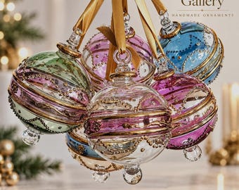 May include: A cluster of round glass ornaments tied with a gold ribbon, featuring green, pink, and blue hues with gold-painted swirls and beaded accents. The text Arabazaar Gallery Handmade Ornaments is visible at the top right.