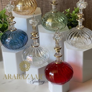 Puede incluir: Seis botellas de vidrio decorativas con tapones dorados y un diseño texturizado y acanalado. Las botellas se muestran sobre bases hexagonales blancas. Las botellas son de varios colores, incluyendo transparente, rojo, verde, azul y rosa.