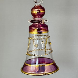 May include: A purple glass Christmas bauble shaped like a bell with gold trim and a clear glass top. The bauble has a loop at the top for hanging.