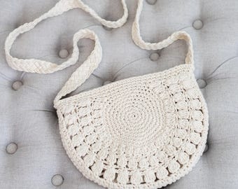 May include: A white crocheted bag with a round bottom and a long strap. The bag is made of a delicate, open-weave material.