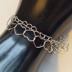 May include: A silver bracelet with a chain made of interconnected heart shapes.