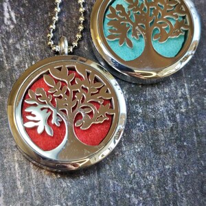 May include: Two circular silver-toned metal locket necklaces featuring a cut-out tree design. One locket contains a bright red felt insert, while the other locket features a vibrant turquoise felt insert. Both pendants hang from silver ball chains.