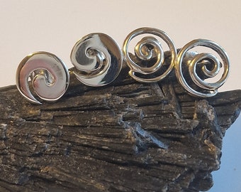May include: Four silver spiral earrings on a dark gray rock surface.
