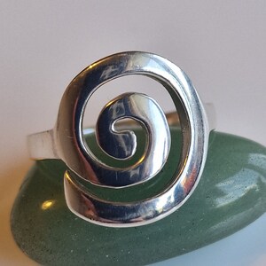 May include: A silver ring featuring a spiral design. The ring is resting on a green stone.