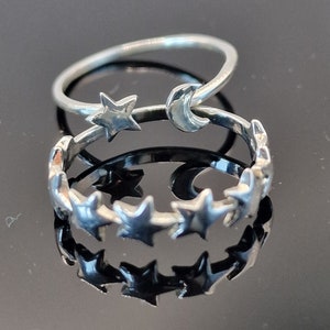 May include: Two silver rings, one with a crescent moon and star design, and the other with a row of stars.