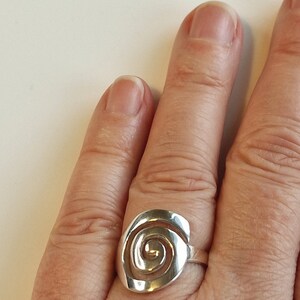 May include: A silver ring featuring a spiral design. The ring is worn on a finger.
