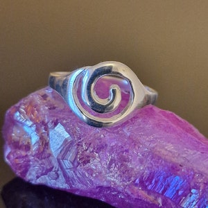 May include: A silver ring with a spiral design. The ring is sitting on a purple crystal.