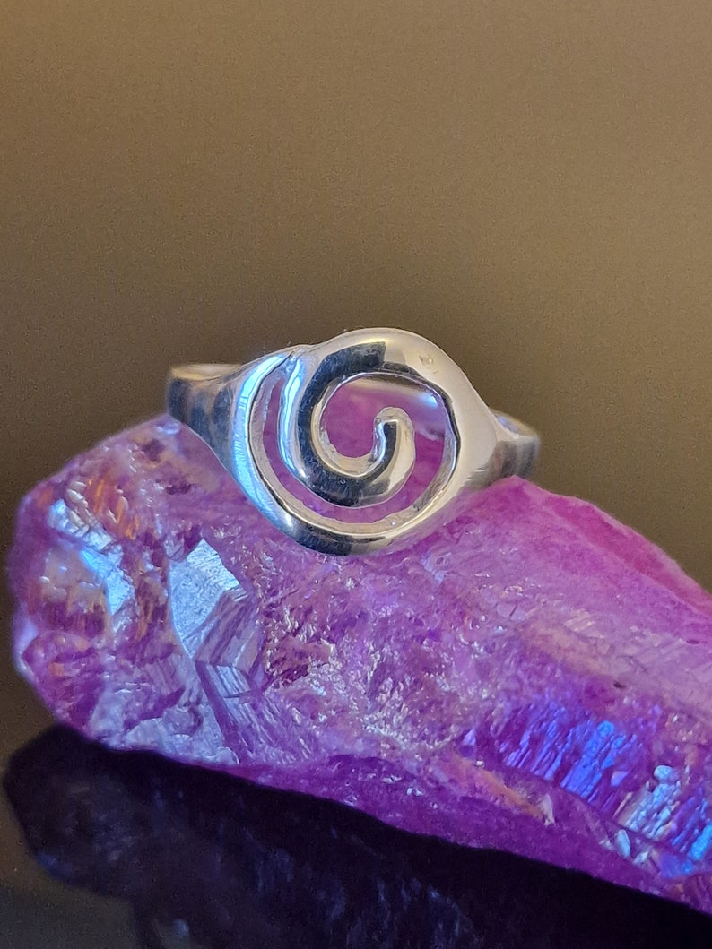 May include: A silver ring with a spiral design. The ring is sitting on a purple crystal.