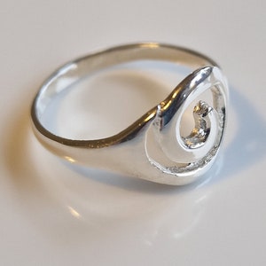 May include: A silver ring with a swirl design. The ring is simple and elegant.