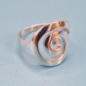 May include: A silver ring featuring a spiral design. The ring is made of metal and has a smooth finish.