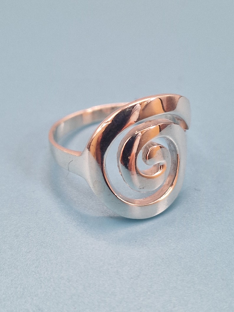 May include: A silver ring featuring a spiral design. The ring is made of metal and has a smooth finish.