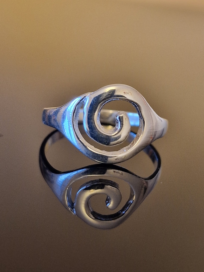 May include: A silver ring with a spiral design. The ring is made of metal and has a smooth finish.