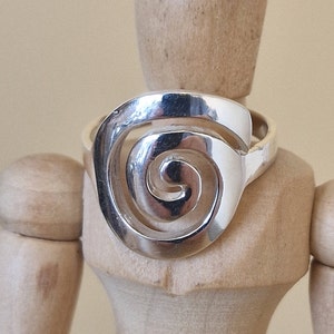 May include: A silver ring featuring a spiral design. The ring is displayed on a wooden mannequin.