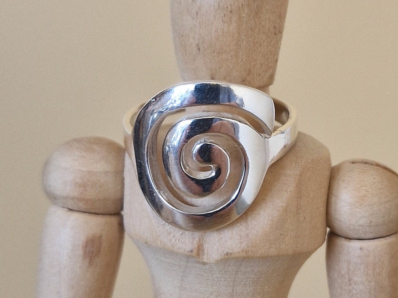 May include: A silver ring featuring a spiral design. The ring is displayed on a wooden mannequin.