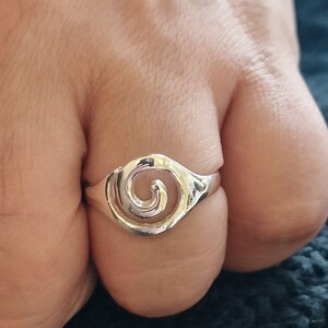 May include: A silver ring with a swirl design. The ring is on a person's finger.