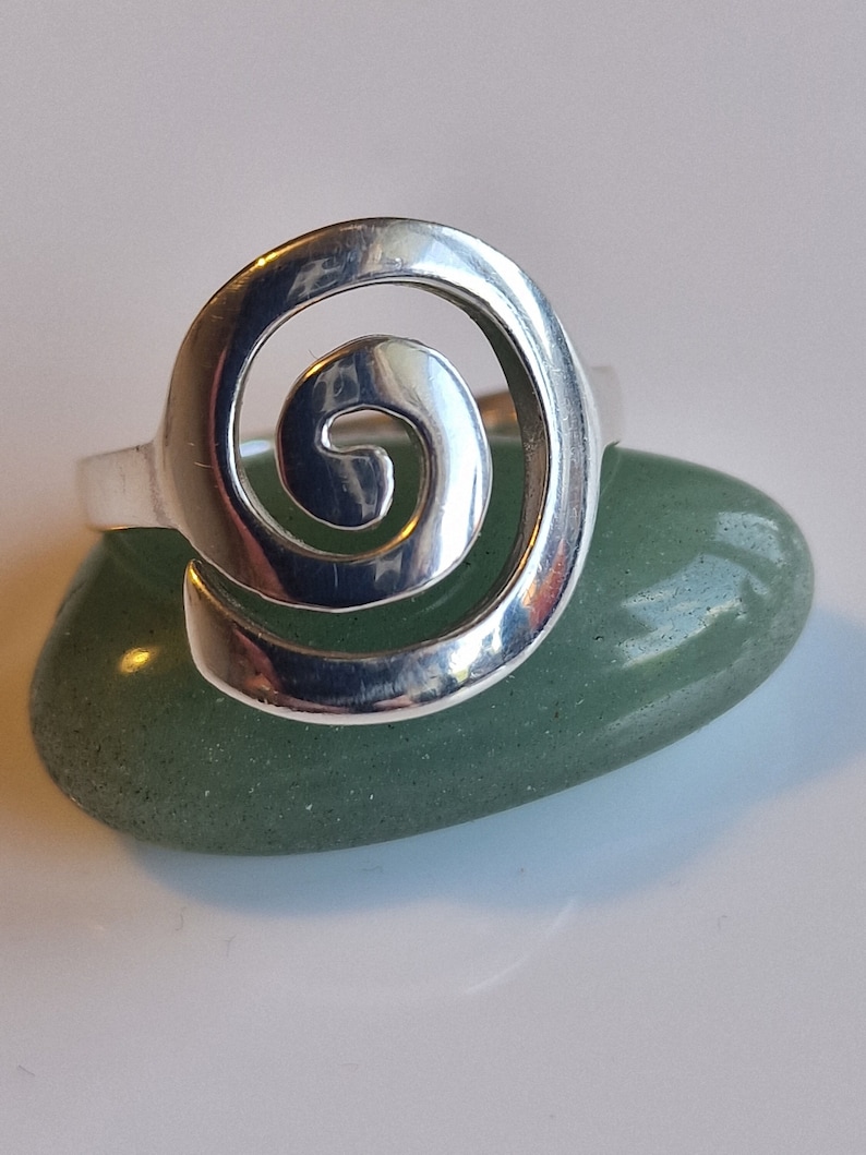 May include: A silver ring featuring a spiral design. The ring is resting on a green stone.