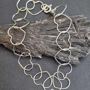 May include: A silver bracelet made of interconnected heart-shaped links. The bracelet is laid out on a dark grey surface.