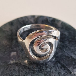 May include: A silver ring featuring a spiral design. The ring is displayed on a dark grey background.