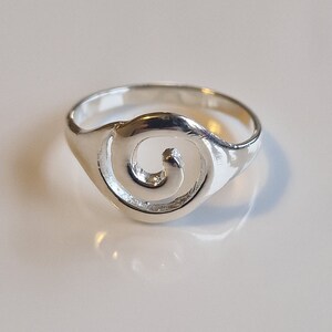 May include: A silver ring with a swirl design. The ring is simple and elegant.