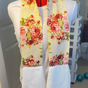 May include: A white kitchen towel with a floral print and white waffle weave fabric. The towel is tied around a red and white mannequin.