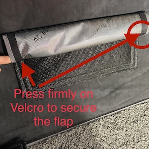 May include: A black fabric flap with a gray mesh pocket and a red arrow pointing to the velcro closure. The text "Press firmly on Velcro to secure the flap" is written below the pocket.