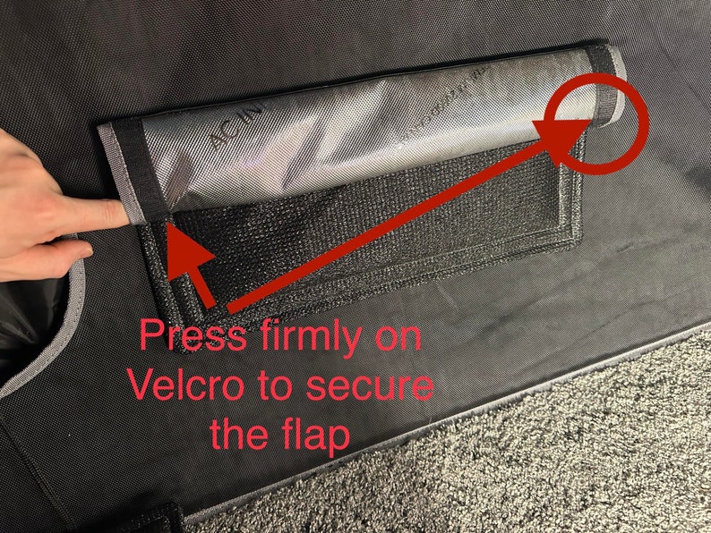 May include: A black fabric flap with a gray mesh pocket and a red arrow pointing to the velcro closure. The text "Press firmly on Velcro to secure the flap" is written below the pocket.