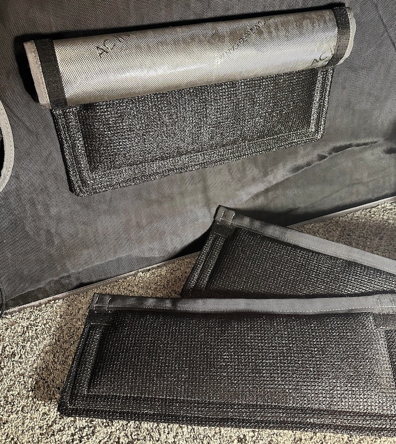 May include: Two black mesh storage pockets with black trim. The pockets are attached to a black fabric surface.