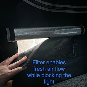 May include: A black grow tent with a zippered opening. A white mesh filter is visible inside the tent. The text "Filter enables fresh air flow while blocking the light" is written on the tent.