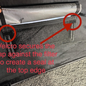 May include: A black fabric filter with a gray flap that secures with velcro. The flap has a mesh pocket and a silver lining. The text "Velcro secures the flap against the filter to create a seal at the top edge" is written below the filter.