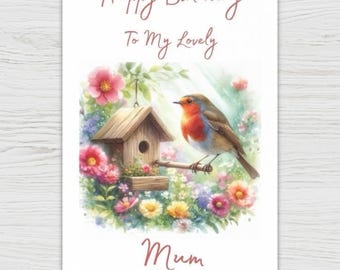 Può includere: Biglietto di compleanno con illustrazione ad acquerello. Raffigura un uccello appollaiato vicino a una casetta per uccelli, circondato da fiori colorati. Il testo recita: "Happy Birthday To My Lovely Mum".