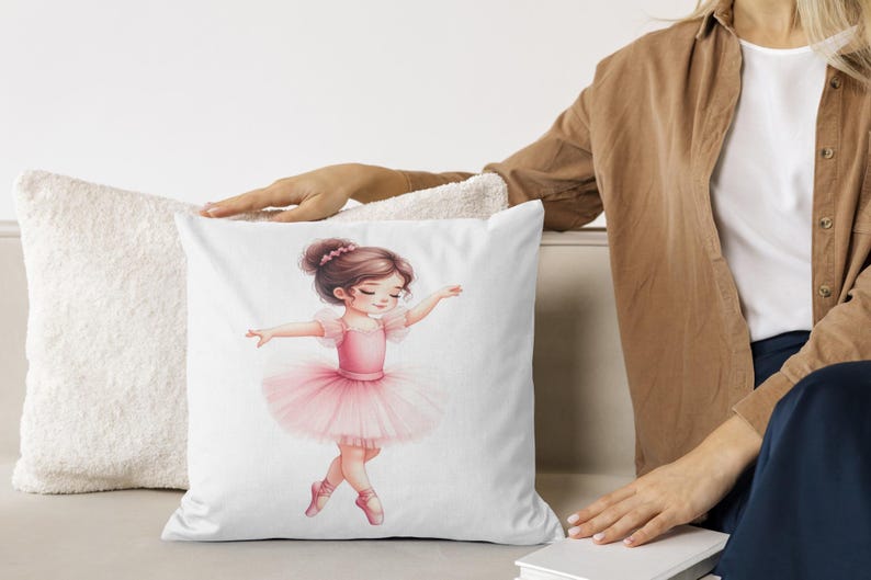 Op de afbeelding: Wit vierkant kussen met een aquarel illustratie van een jonge ballerina in een roze tutu en balletschoenen. De ballerina heeft bruin haar en staat in een sierlijke pose, armen uitgestrekt. Het kussen ligt op een licht oppervlak.