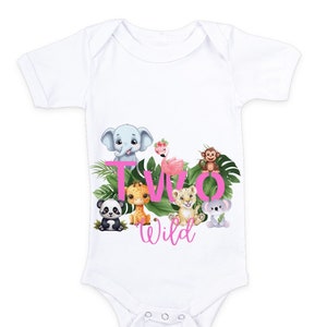 K&ouml;nnte beinhalten: Wei&szlig;er Baby-Strampler mit einem pinkfarbenen 'Two Wild'-Motiv, das verschiedene Dschungeltiere zeigt, darunter einen Elefanten, eine Giraffe, einen L&ouml;wen, einen Affen, einen Panda und einen Flamingo.