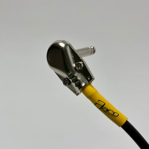 May include: A close-up of a right-angle guitar cable with a yellow outer sheath and a black inner cable. The cable is labeled "Jaco" in black text. The cable has a silver metal connector.