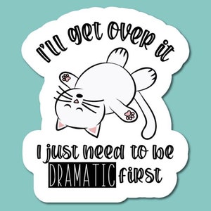 May include: A white sticker with a cartoon cat lying on its back. The sticker has the text "I'll get over it, I just need to be DRAMATIC first" in a playful font. The cat has pink ears and paw pads.