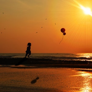 Sunset child chasing balloons on beach