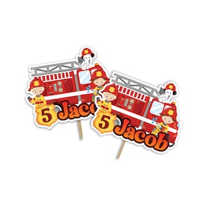 May include: Two red fire truck cake toppers with a fireman and dalmatian dog. The toppers are personalized with the name "Jacob" and the number "5".