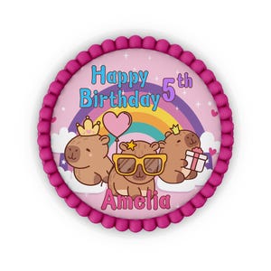 May include: A round cake topper featuring three brown capybaras on a pink background with a rainbow, stars, and hearts. The text reads Happy Birthday 5th Amelia. The capybaras wear crowns, sunglasses, and hold a heart balloon and gift box.