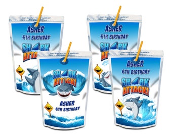 May include: Four juice boxes with a shark theme. Each box displays a cartoon shark, ocean waves, and the text "SHARK ATTACK!" and "ASHER 6TH BIRTHDAY." The boxes are blue and white with yellow straws.