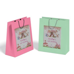 Puede incluir: Dos bolsas de regalo con asas, una rosa y otra verde. Ambas bolsas presentan un diseño impreso de hadas y una casa en el árbol con el texto "Evelyn's 2nd Birthday".