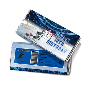 Puede incluir: Un envoltorio de barra de chocolate azul y blanco con temática de hockey. El envoltorio presenta a un jugador de hockey patinando en una pista de hielo, un palo de hockey y una portería de hockey. El texto en el envoltorio dice "Ethan 10th Birthday" y "Gracias por celebrar conmigo".