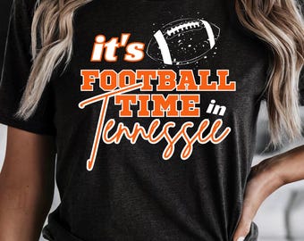 Puede incluir: Camiseta gris oscuro con el texto "it's FOOTBALL TIME in Tennessee" en naranja y blanco. Un gráfico de fútbol americano blanco está encima del texto. La camiseta es de estilo casual.